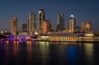 A city skyline at night with lights reflecting off the water.